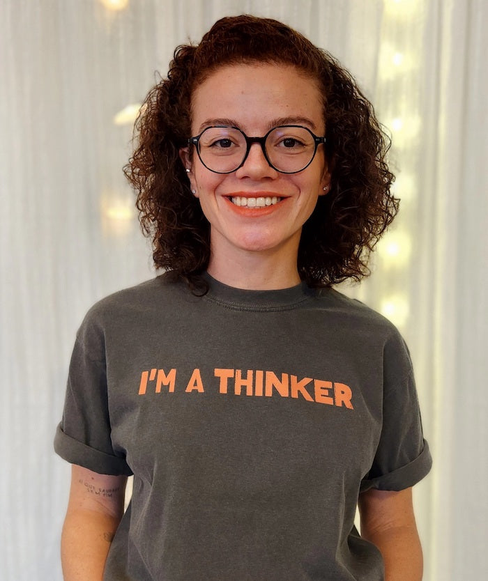 A person proudly wears a t-shirt saying I’m a Thinker, emphasizing the need to rethink oppressive social systems.